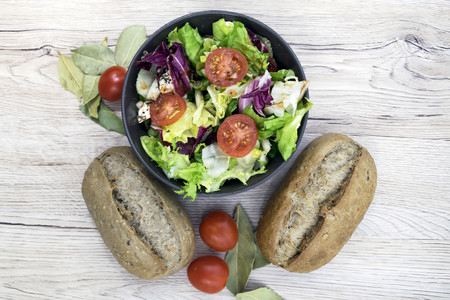 Fresh vegetarian breakfast prepared on the wooden background. Salad with cherry tomatoes, feta cheese, lettuce, onion and garlic with barbecue sauce. Two fresh bread rolls with seeds. Top view.の写真素材