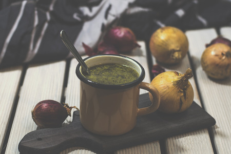 French onion soup in the enamelled mug. White wooden background. Wooden cutting boardの写真素材