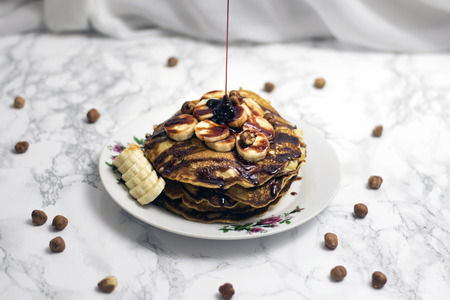 American pancakes with maple sauce, bananas and hazelnuts. White marble Christmas background