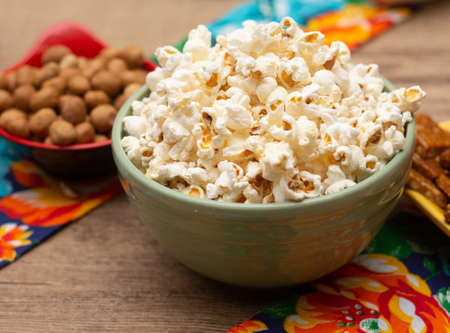 big bowl with popcorn surrounded by peanuts and candies on the tableの写真素材