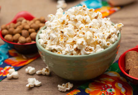 big bowl with popcorn surrounded by peanuts and candies on the tableの写真素材