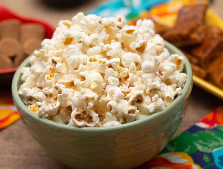 big bowl with popcorn surrounded by peanuts and candies on the tableの写真素材