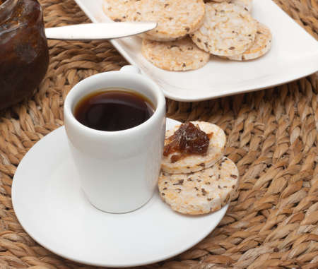A cup of coffee under the straw table surrounded by a bowl full of rice cookies and a jelly potの写真素材