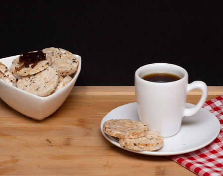 a cup of coffee beside a rice vegan cookies with jelly on the top and a bowl full of rice cookiesの写真素材