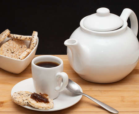 a cup of coffee surrounded by a bowl full of rice cookies and a coffee potの写真素材