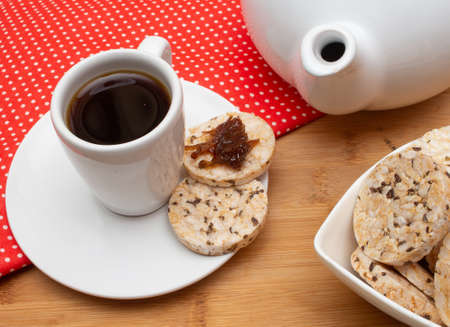 A cup of coffee under the straw table surrounded by a bowl full of rice cookies and a coffee potの写真素材