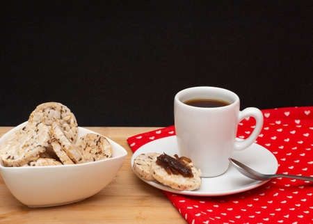 a cup of coffee beside a spoon and a bowl full of rice vegan cookies with jelly on the topの写真素材