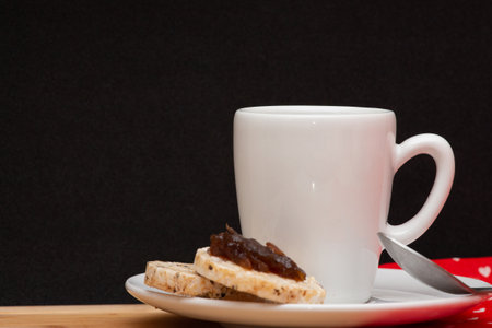 a cup of coffee beside a spoon and a vegan rice cookies with a jelly on the topの写真素材