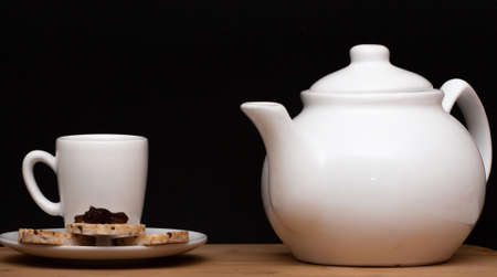 cup of coffee beside rice vegan cookies with jelly on the top and a coffee pot under the wood tableの写真素材