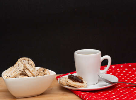 a cup of coffee beside a spoon and a bowl full of rice vegan cookies with jelly on the topの写真素材