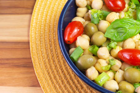 top view of chickpeas with leaves, olives and tomatoes in a blue bowl on the tableの写真素材
