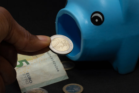 hand holding a one euro coin and putting it in piggy bankの写真素材