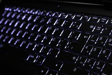 Close-up of a laptop keyboard with purple lights in the backgroundの写真素材