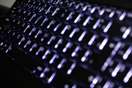 Close up of a computer keyboard in a dark room with purple lightsの写真素材