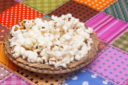 Popcorn in a wooden bowl on a colorful tablecloth background.の写真素材