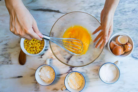 Unrecognizable woman cooking corn pie with ingredients on a marble tableの写真素材
