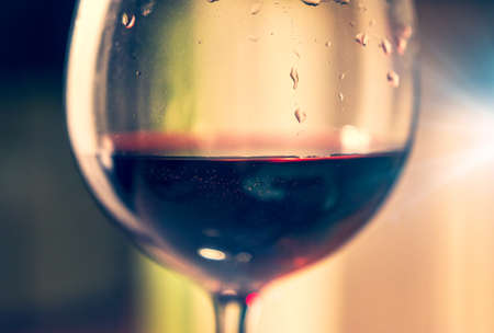 A glass of red wine illuminated by light with a colored blurred background