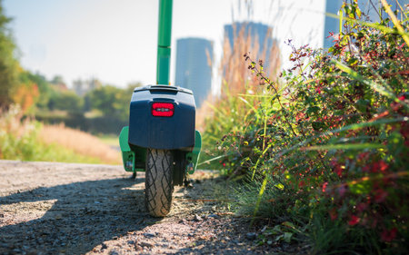 The electric green scooter stands on a dirt path among ornamental grasses. Red light mounted on the back of the scooterの写真素材
