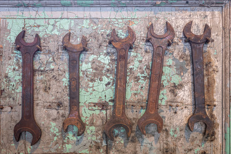 Five old, rusted wrench tools hanging on nails on cracked, damaged wall.の写真素材