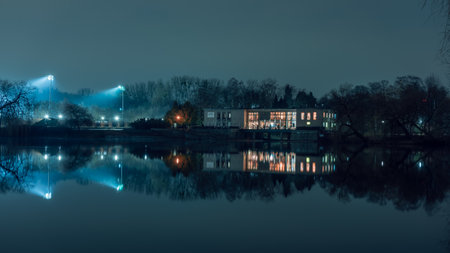 ChorzÃ³w, Poland - February 23, 2023: Silesian Park in ChorzÃ³w. Evening view towards the cafe located on the shore of the pond. Illuminated cafe interiors. moody scenery.のeditorial素材