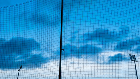 Football pitch fencing in the form of a protective net. Ball catcher. Silhouette of stadium spotlights against the blue sky. Blue hourの写真素材
