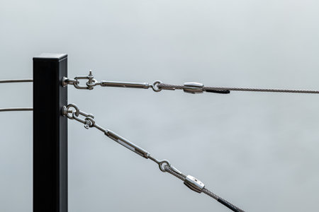 Balustrade made of stainless steel cable attached with a turnbuckle and hooks to a graphite-colored steel postの写真素材