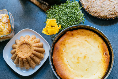 Holiday baking. Pound cake and cheesecake in a baking tin surrounded by a green plant, a yellow flower on an anthracite countertop.の写真素材