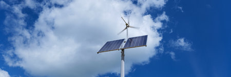 Photovoltaic panel with a small windmill on a street light pole against a blue sky with few clouds. Energy from wind and sun.の写真素材