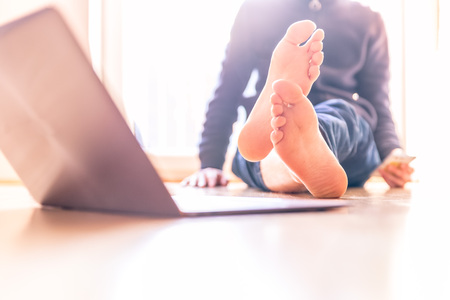 Barenaked young man is sitting on the wooden floor and enjoys the day, laptop in the foregroundの写真素材