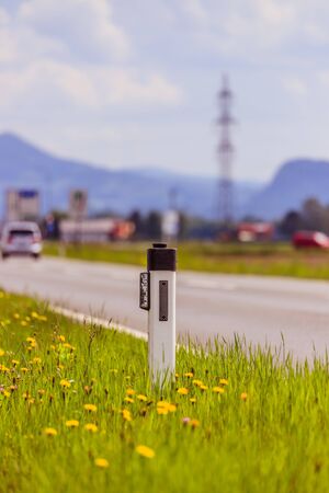 Reflector post and cars at an idyllic asphalted road in summer, flowers and green grassの写真素材