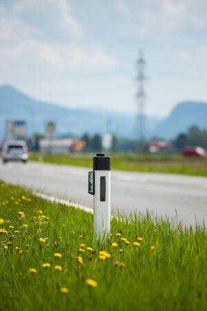 Reflector post and cars at an idyllic asphalted road in summer, flowers and green grassの写真素材