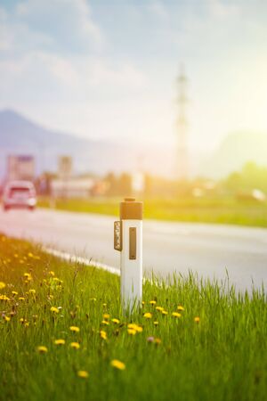 Reflector post and cars at an idyllic asphalted road in summer, flowers and green grassの写真素材