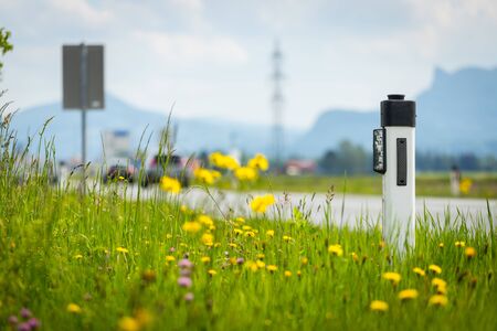 Reflector post at an idyllic asphalted road in summer, flowers and green grassの写真素材