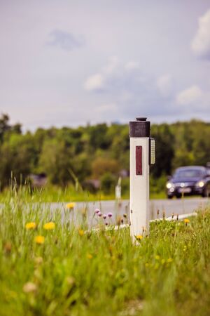 Reflector post and cars at an idyllic asphalted road in summer, flowers and green grassの写真素材