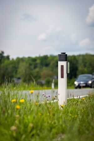 Reflector post and cars at an idyllic asphalted road in summer, flowers and green grassの写真素材