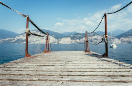 Wooden dock pier extending over blue lake water, mountains at lago di garda. Text space.の写真素材