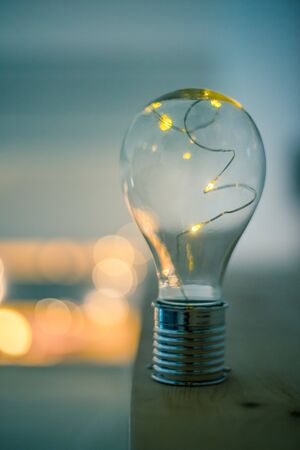 LED light bulb is lying on a wooden table. Symbol for ideas and innovation. Spot lights in the blurry background.の写真素材