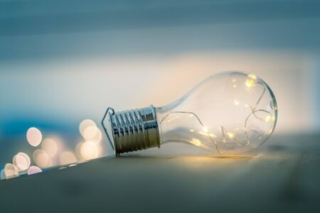 LED light bulb is lying on a wooden table. Symbol for ideas and innovation. Spot lights in the blurry background.の写真素材