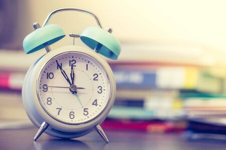 Alarm clock is standing on a grey desk, books and office stuff in the blurry backgroundの写真素材