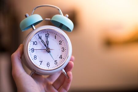 Man is holding an alarm clock, sunshine in the morning, blurry backgroundの写真素材
