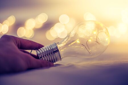 LED light bulb is lying in the bed, hands touching. Symbol for ideas and innovation. Spot lights in...