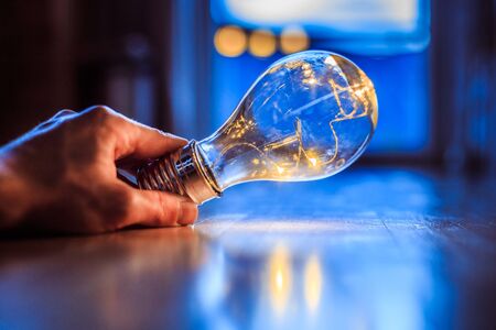 Hands are holding a LED lightbulb over the wooden floor. Symbol for ideas and innovation. Window and light in the blurry background.の写真素材