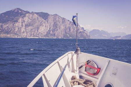 Bow of a boat on a boat tour. Blue water and mountain range, Lago di Garda, Italyの写真素材
