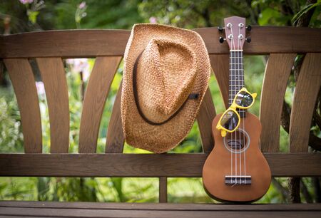 Ukulele and yellow sunglasses on a wooden park bench in summer, green area in the blurry backgroundの写真素材