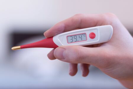 Man holds a red fever thermometer with 39 degrees Celsius in his handの写真素材