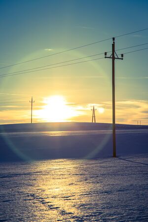 Electrical tower on a snowy field in Austria, sunset sceneryの写真素材