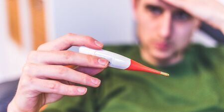 Man is holding a red fever thermometer in his hand