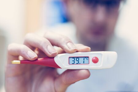 Man is holding a red fever thermometer in his hand