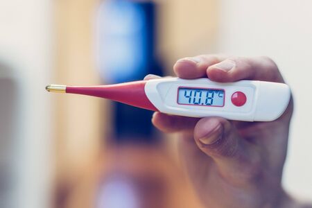 Man is holding a red fever thermometer in his hand