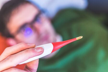 Man is holding a red fever thermometer in his hand